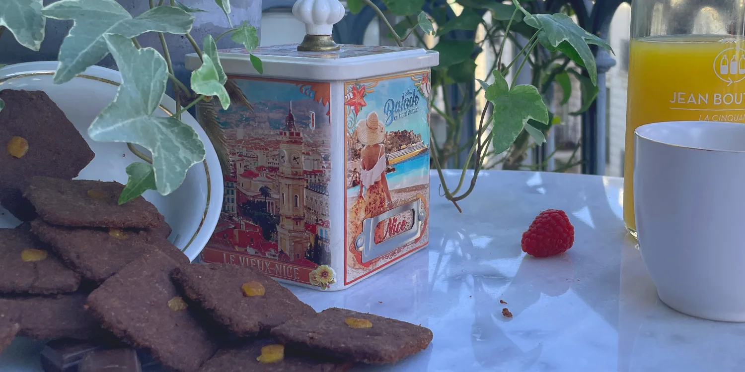 biscuits le précieux tout chocolat avec de l'orange confite mis en scène sur un balcon avec une tasse de thé, une framboise et du jus de fruit